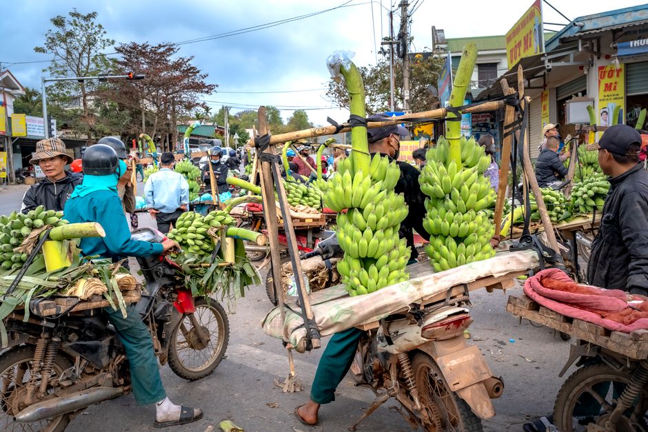 A lively Southeast Asian street market with motorbike vendors selling fresh bananas.