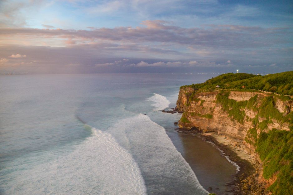 Breathtaking aerial view of Uluwatu cliffs in Bali with vibrant ocean waves during sunset.