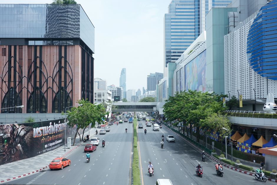 Vibrant city street in Bangkok featuring modern architecture, traffic, and urban greenery.