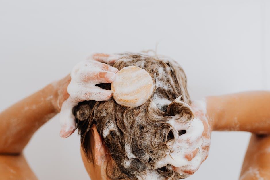 Close-up of a person washing their hair with soap bar and foam, focusing on hands and hair.