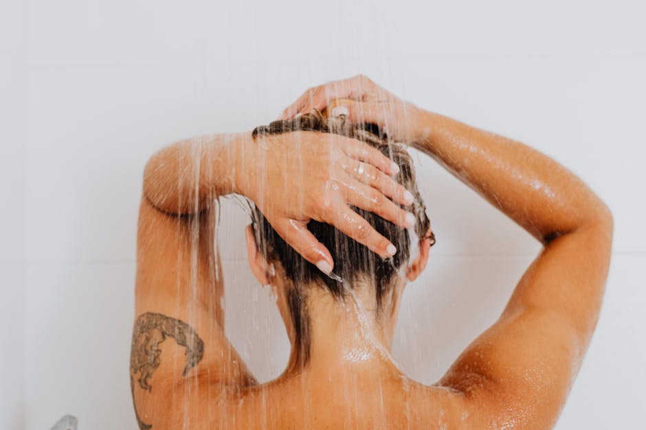 Person taking a shower, showcasing a tattoo on the arm and water flowing down.