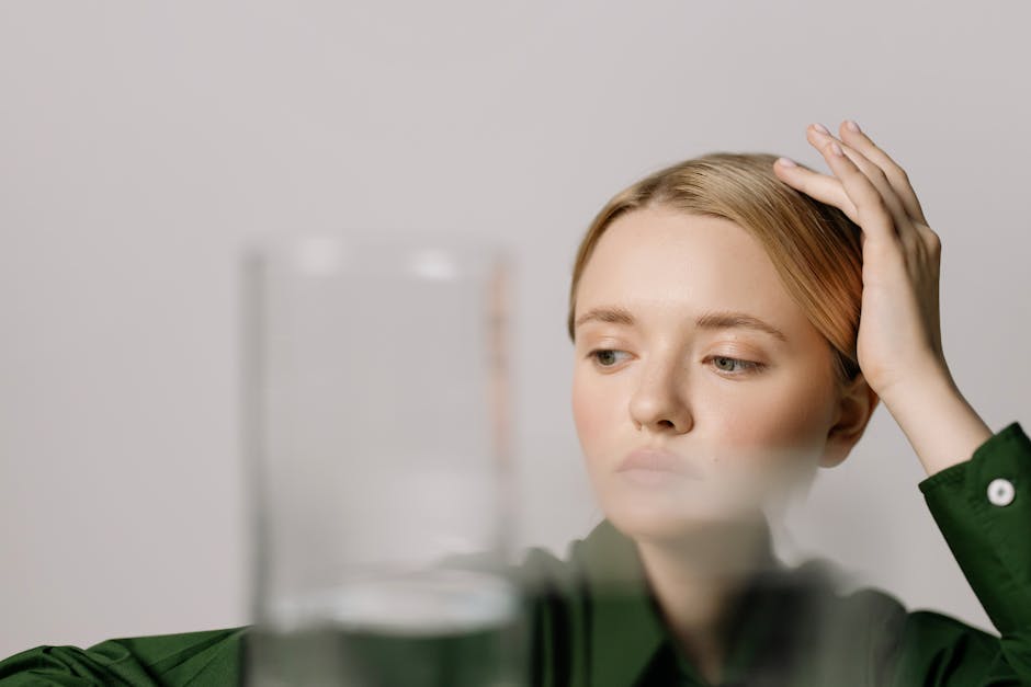 Woman contemplating with a glass of water in foreground, serene setting.