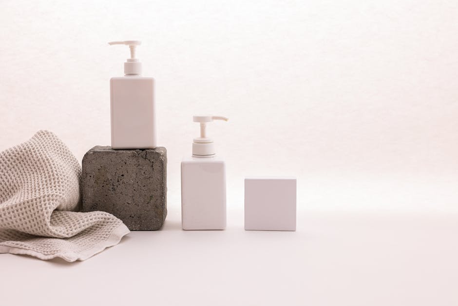 Stylish minimalist setup with cosmetic pump bottles and fabric on a white background, ideal for beauty product presentation.
