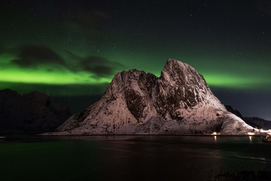 Breathtaking view of the Northern Lights over a snow-covered mountain by night.