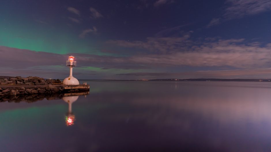 A serene lighthouse illuminated at dusk, reflecting on calm sea waters under a starry sky.