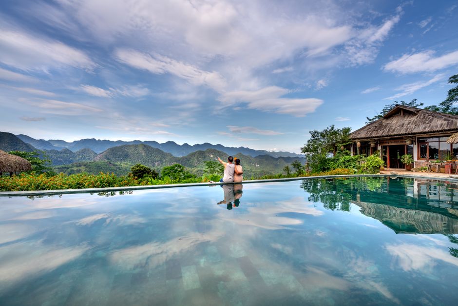 Couple enjoying a scenic view from an infinity pool with lush mountains and blue sky.