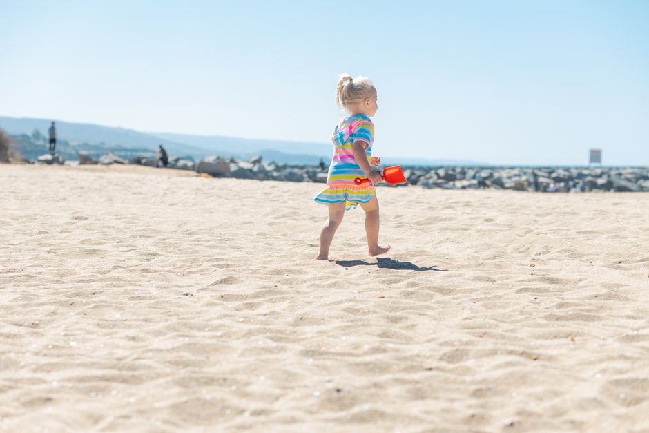 Adorable child in colorful dress enjoying a sunny day at the beach with a bright sand toy.