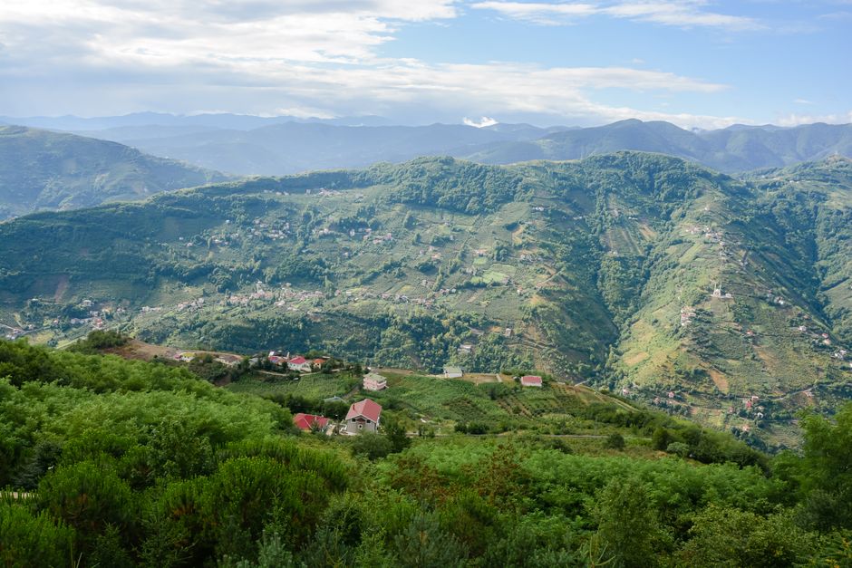 A breathtaking panoramic view of lush green mountains and scattered rural houses under a bright sky.