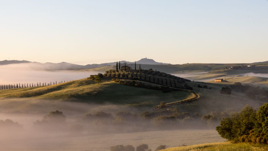 Enchanting sunrise view of mist-covered Tuscan hills and iconic cypress trees.