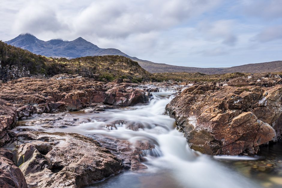 Beautiful Scottish Highland waterfall with rocky landscape and distant mountains.