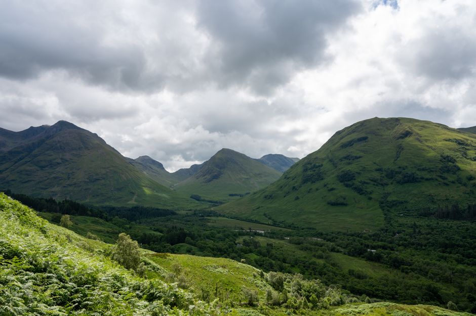 Explore the lush, green valleys and rolling hills of the Scottish Highlands under a cloudy summer sky.