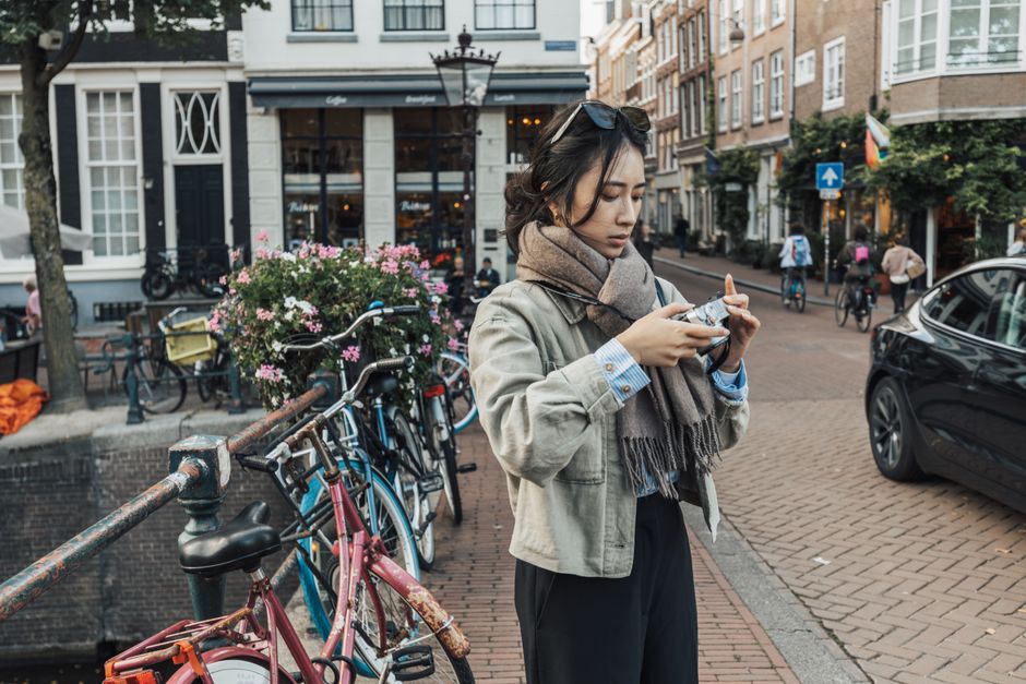 A woman stands with a camera on a bustling Amsterdam street lined with bicycles and charming architecture.