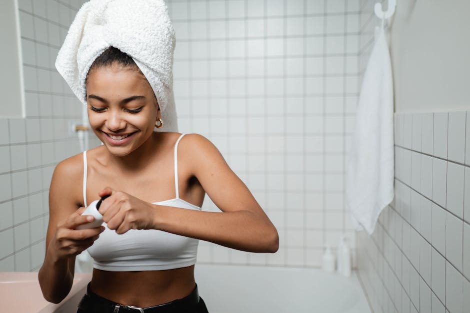 A young woman with a towel on her head enjoys her skincare routine in a modern bathroom.