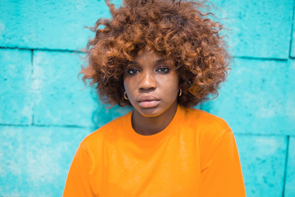 Vibrant portrait of a young woman with curly hair and orange top against a blue wall.