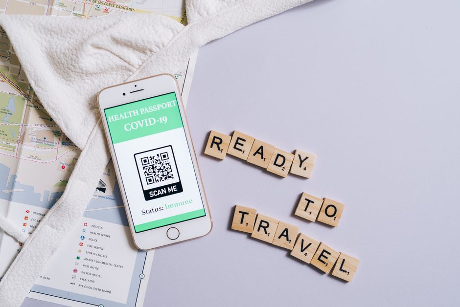 A smartphone showing a COVID-19 health passport next to Scrabble letters spelling 'Ready to Travel'.
