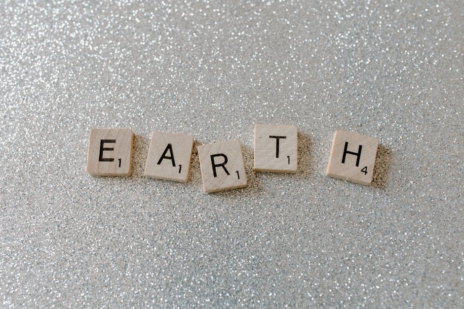 Wooden Scrabble tiles spelling 'EARTH' on a sparkling glitter background.