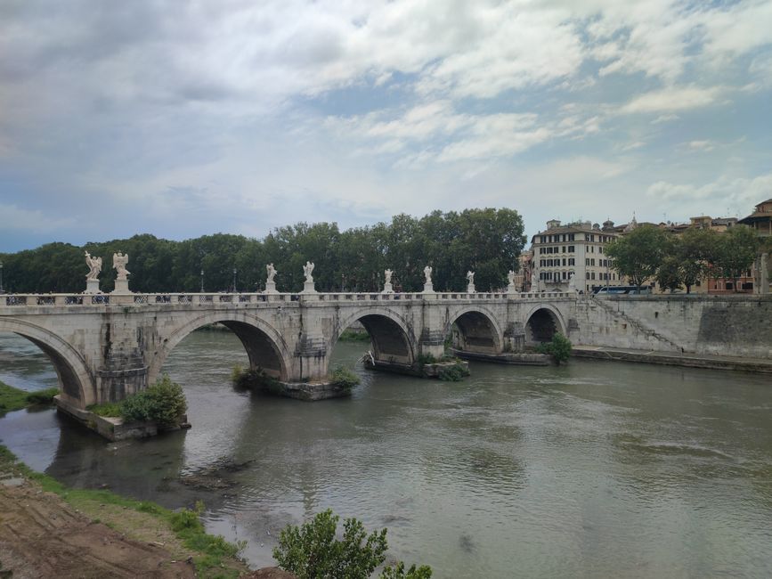 View of the iconic Ponte Sant'Angelo crossing the Tiber River in Rome, Italy, on a cloudy day.