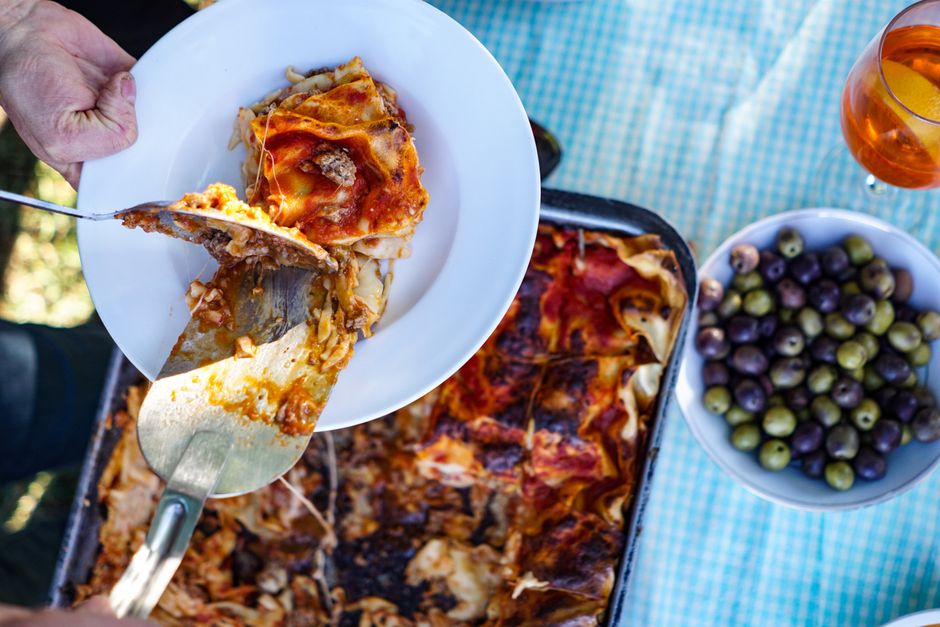 A delicious slice of homemade lasagna being served on a white plate, accompanied by olives.