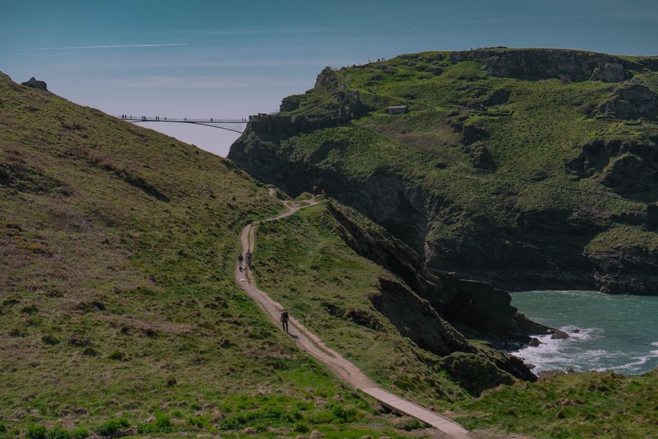 Lush landscape with a scenic path leading to Tintagel Castle Bridge in England.