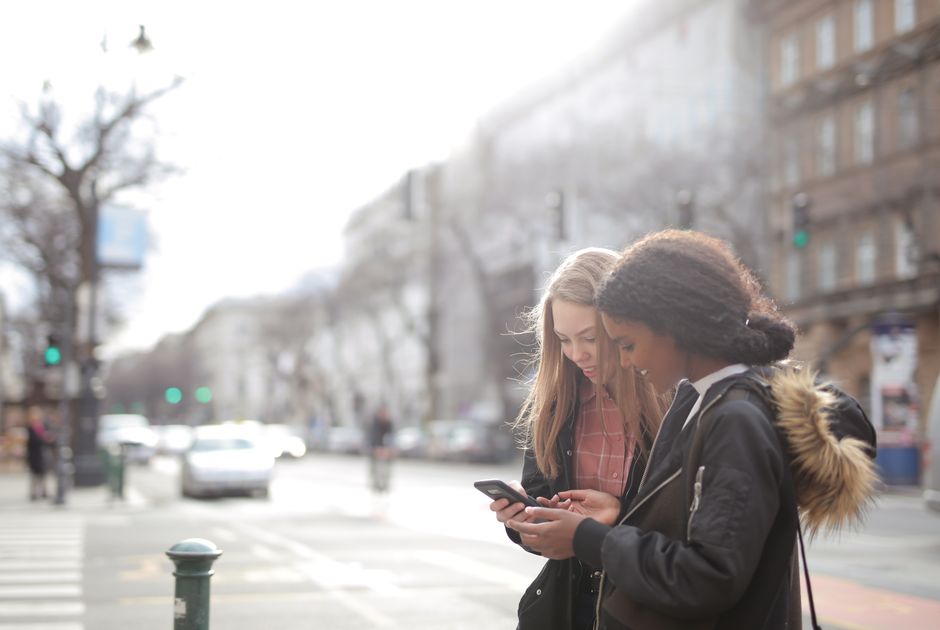 Two young women looking at a smartphone on a bustling urban street during the day.