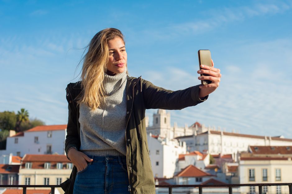 Young woman taking a selfie outdoors in a picturesque European city setting.