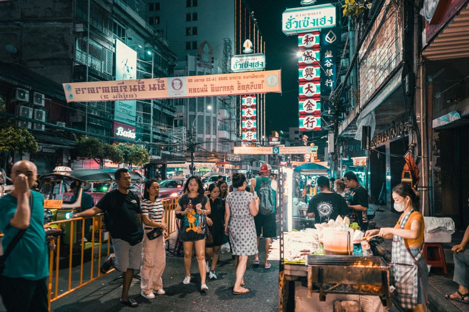 Explore the vibrant street market in an Asian city at night filled with people and neon lights.