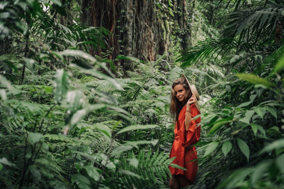 Stylish woman posing in a vibrant green jungle setting, surrounded by lush plants.