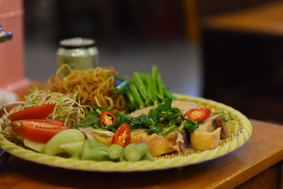 A colorful Vietnamese platter featuring vegetables, herbs, and cooked chicken garnished with chili.