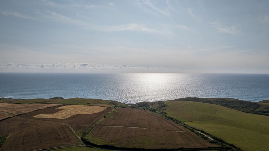 Stunning aerial view of Bude's coastline and fields in Cornwall, England, against a clear blue sky.