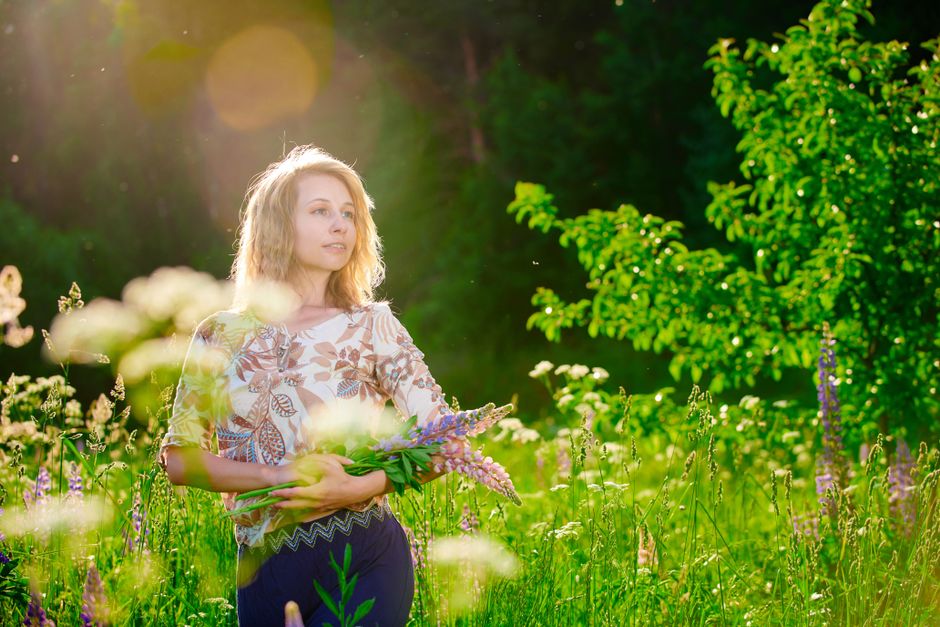 A woman enjoys the sunshine in a lush flower field, holding wildflowers.